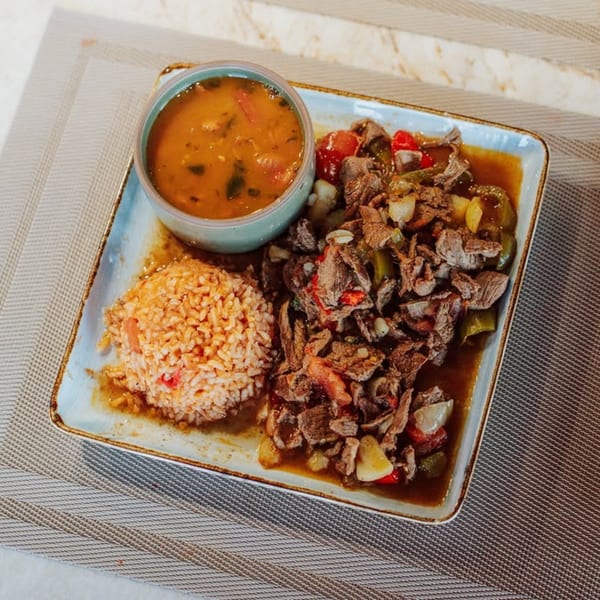 A plate of beef stew with peppers and onions, a side of rice, and a bowl of soup.