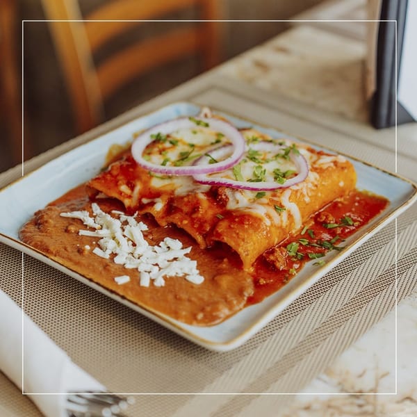 Two enchiladas covered in red sauce, cheese, red onion, and cilantro, served with refried beans.