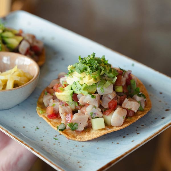 A Cosmos Bar & Grill ceviche tostada with avocado, cilantro, and a side of plantain chips.