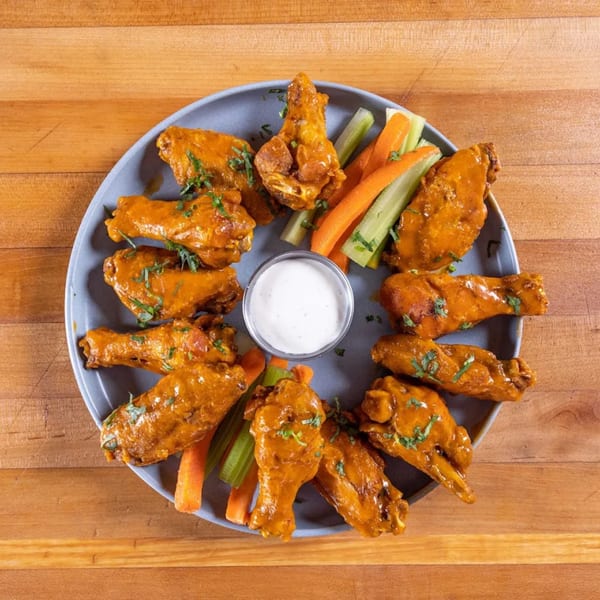 A plate of Cosmos Bar & Grill's buffalo wings with celery, carrots, and ranch dressing.