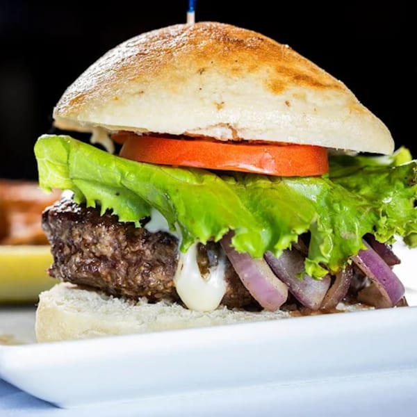 A Cosmos Bar & Grill burger with a thick patty, lettuce, tomato, onions, and sauce.