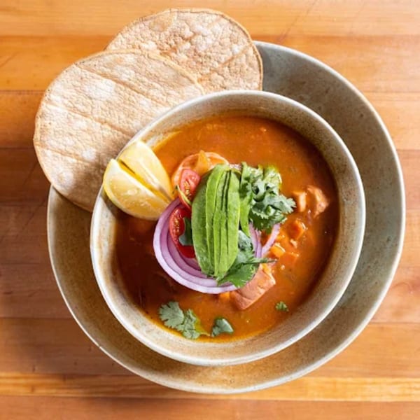 Hearty red soup with avocado, red onion, cilantro, and lemon, served with tortillas.