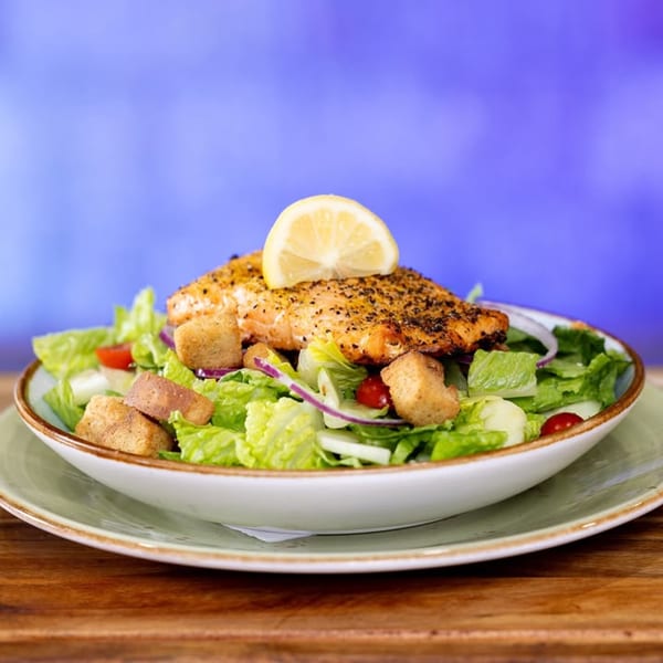 Cosmos Bar & Grill's grilled salmon salad with lettuce, tomatoes, croutons, and a lemon slice.