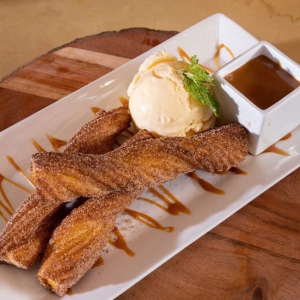 Cosmos Bar & Grill churros with vanilla ice cream, mint, and caramel sauce on a white plate.
