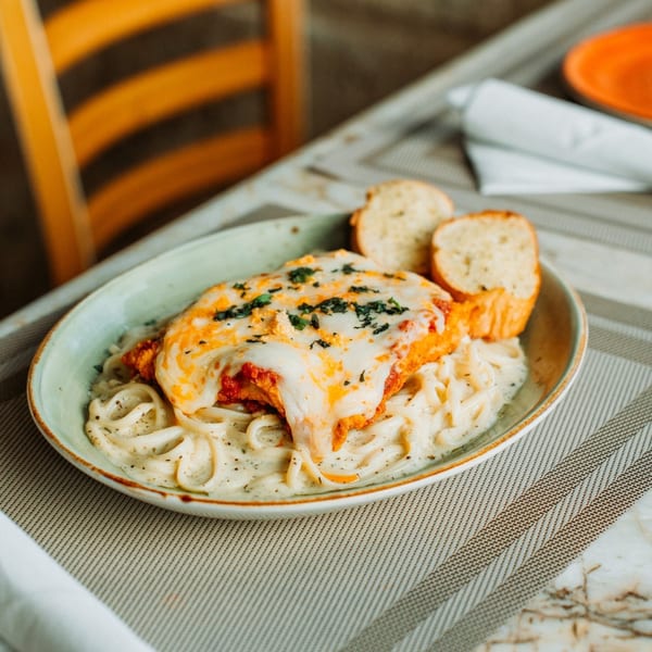Chicken parmesan with creamy pasta and garlic bread on a striped placemat at Cosmos Bar & Grill.
