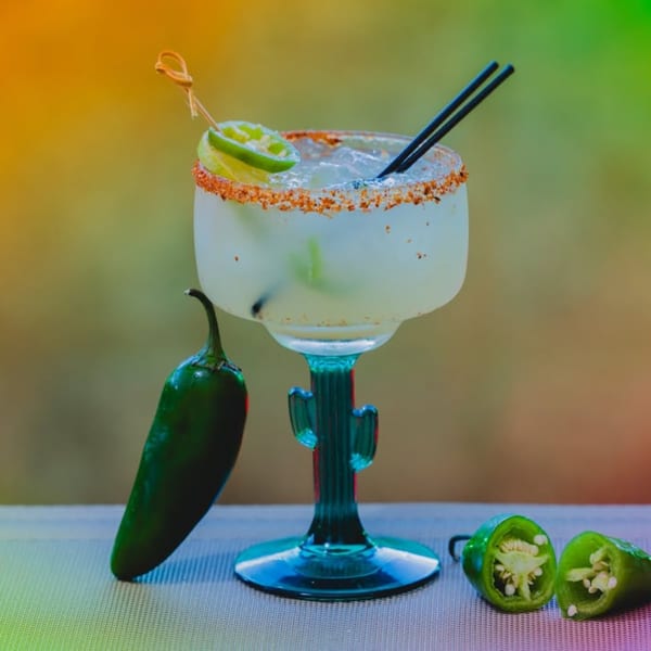 Spicy margarita in a cactus-stemmed glass with lime and jalapeños on a colorful background.