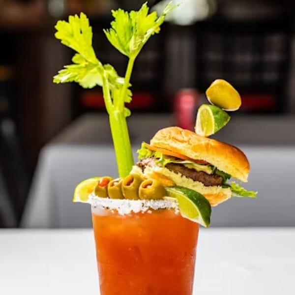 A Bloody Mary cocktail garnished with celery, olives, lime, lemon, and a mini burger.